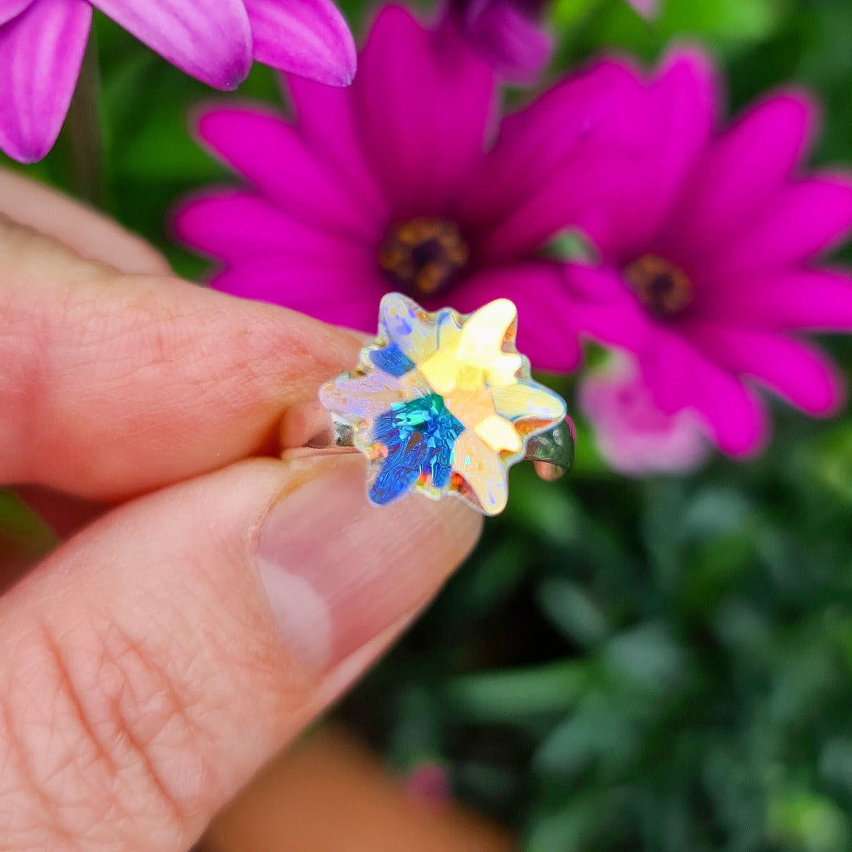 Close-up of Edelweiss-Shaped Crystal in Aurora Borealis on Silver Ring on a floral background